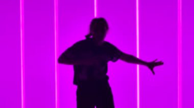 Aktif bir dansçı stüdyoda neon tüplerin arka planına karşı modern koreografiyi gösterir. Kız serbest stil dansını yavaş çekimde gösteriyor. Siluet. Kapat..