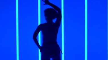 Stüdyoda çok renkli neon tüplerin arka planında çağdaş dans eden bir kadının silueti. Dansçı kollarını ve kalçalarını düzgün ve zarifçe hareket ettirir. Ağır çekim. Kapat..