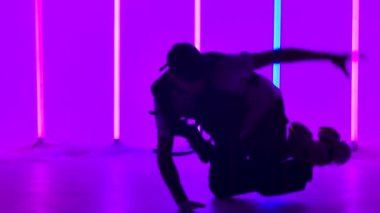 Adam stüdyoda çok renkli neon lambaların arka planında breakdance yapıyor. Siluet. Sokak dansı bir yaşam biçimidir. Kapatın. Yavaş çekim.