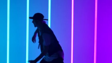 Profesyonel Hip Hop break dansçısı. Çok renkli neon ışıklar arasında dans eden şık genç adam çeşitli serbest dans figürleri sergiliyor. Siluet. Kapatın. Yavaş çekim.
