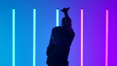 Stüdyoda neon ışıklarının önünde dans eden beyaz dansçı. Genç adam serbest stil yapıyor. Siluet. Kapatın. Yavaş çekim.