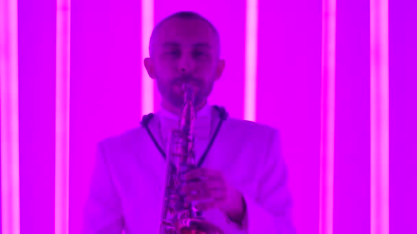 En man spelar saxofon i studion mot bakgrund av flerfärgade neonrör. Live föreställning. Jazzmusik. Klubbmusik. Långsam rörelse, närbild. — Stockvideo