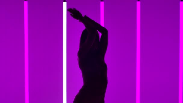 Silhuett av en dansande flicka i studion mot bakgrund av ljusa flerfärgade neonrör. Flickan dansar samtida, stora rörelser hennes höfter och händer i slow motion. Närbild. — Stockvideo