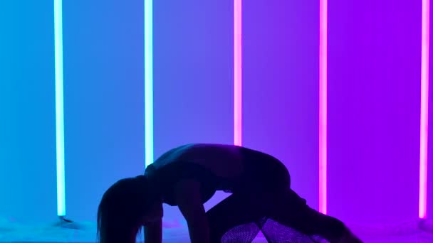 Silueta dívčí tanečnice provádějící akrobatické prvky současné choreografie. Umělec tančí ve studiu na pozadí modrých a růžových neonových trubic ve zpomaleném filmu. Zavřít. — Stock video