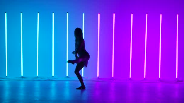 Silhouette of a dancing girl in the studio against the background of bright multicolored neon tubes. A professional ballerina dances modern choreography with ballet elements in slow motion. — Stock Video