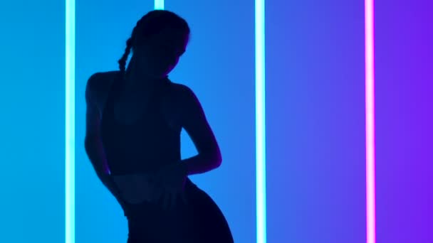 Stüdyoda, parlak neon boruların arka planına karşı ağır çekimde hip hop sokak dansı yapan genç bir kadın. Gençlik alt kültürü. Koyu renk siluet. Kapat.. — Stok video