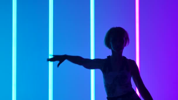 Sylwetka pełnej wdzięku młodej kobiety tańczącej elementy tańca współczesnego w studio na niebieskim fioletowym tle z neonowym oświetleniem w zwolnionym tempie. Zamknij się.. — Wideo stockowe