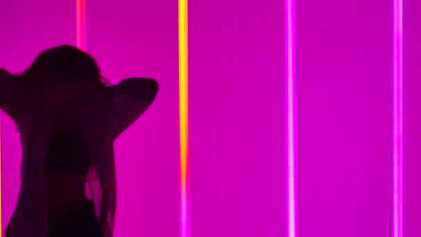 Donna che danza contemporanea in studio sullo sfondo di tubi al neon multicolore. Una ragazza di talento esegue una danza con elementi di modernità e balletto al rallentatore. Silhouette. Primo piano. — Video Stock