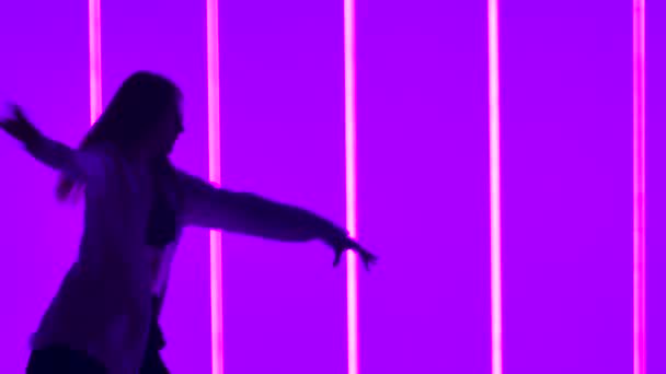 在彩色霓虹灯管的背景下，妇女在演播室里跳着同时代的舞。一个有才华的女孩以慢动作表演带有现代性和芭蕾舞元素的舞蹈.剪影。包扎. — 图库视频影像