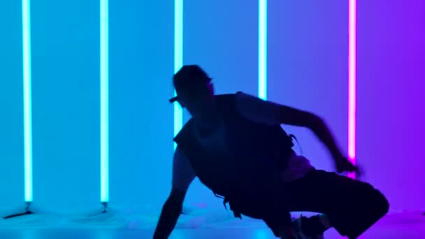 Ballerino hip hop che esegue mosse di danza freestyle. Silhouette di un ragazzo che balla su uno sfondo di luci al neon multicolori nello studio. Chiudete. Rallentatore. — Video Stock
