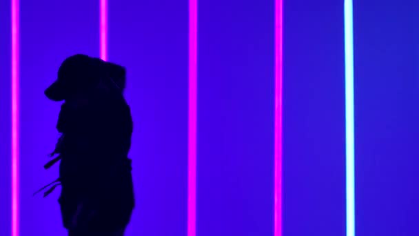 Мужчина танцует хип-хоп в студии на фоне ярких неоновых ламп. Танцовщица практикует танцевальные элементы, выполняя движения фристайла. Силуэт. Закрывай. Медленное движение. — стоковое видео