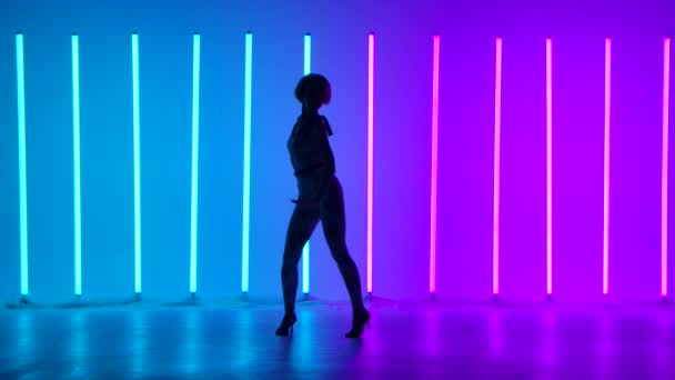 Stüdyoda, neon ışıklı, mavi bir arka planda modern dansın dans öğeleri içinde zarif genç bir kadının silueti. Sokak dansı. Dans posteri tasarımı. Yavaş çekim. — Stok video