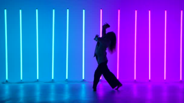 Молодая танцовщица танцует современно в студии на фоне разноцветных неоновых трубок. Танец с элементами современности исполняет талантливая девушка. Силуэт. Медленное движение. — стоковое видео
