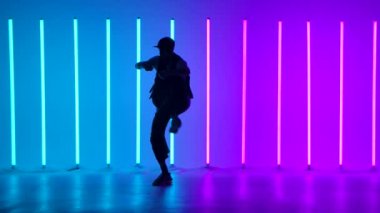 Profesyonel Hip Hop break dansçısı. Çok renkli neon ışıklar arasında dans eden şık genç adam çeşitli serbest dans figürleri sergiliyor. Siluet. Yavaş çekim.