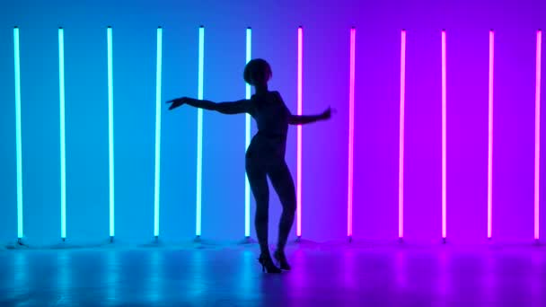 Művészi hölgy bemutatja utcai stílusú koreográfia hátterében sokszínű neon csövek. A lány élvezi a táncot a stúdióban lassítva. Sziluett. — Stock videók