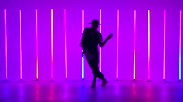 Parlak neon ışıklarının arkasında hip-hop dansı yapan genç bir adam. Günlük gençlik kıyafetleri içinde karmaşık hareketler yapan bir dansçının silüeti. Sokak dansı bir yaşam biçimidir. Yavaş çekim. — Stok video
