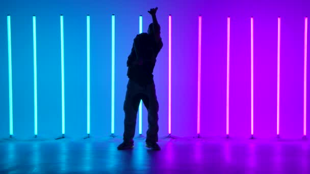 Professional Hip Hop break dancer. Stylish young man dancing among real bright multicolored neon lights performing various freestyle dance moves. Silhouette. Slow motion. — Stock Video