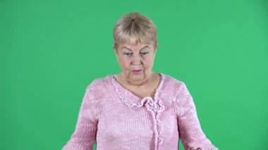 Fotoğraftaki yaşlı kadın kameraya şaşkınlık ve sevinçle bakıyor. Stüdyoda yeşil ekranda pembe kazaklı, kısa saçlı gri saçlı büyükanne. Kapat..