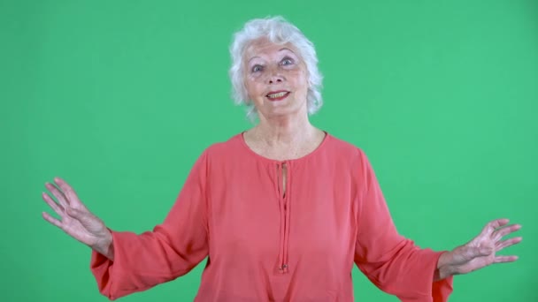 Portret van een oudere vrouw die naar de camera kijkt en glimlacht. Grijze oma in rode blouse op groen scherm in de studio. Sluiten.. — Stockvideo