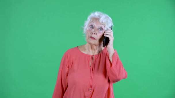 Retrato mujer anciana mirando a la cámara y hablando en su teléfono inteligente. Abuela de pelo gris en blusa roja en pantalla verde en el estudio. De cerca.. — Vídeo de stock