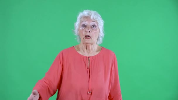 Portret van een oudere vrouw die naar de camera kijkt praat emotioneel met iemand met verontwaardiging. Grijze oma in rode blouse op groen scherm in de studio. Sluiten.. — Stockvideo