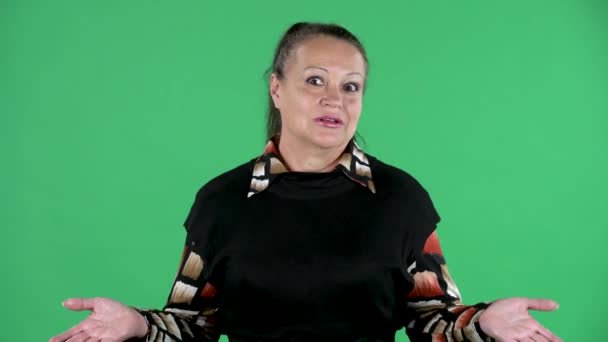 Retrato mujer anciana mirando a la cámara es emocionalmente hablando con alguien con indignación. Morena abuelita en vestido negro en pantalla verde en el estudio. De cerca.. — Vídeos de Stock