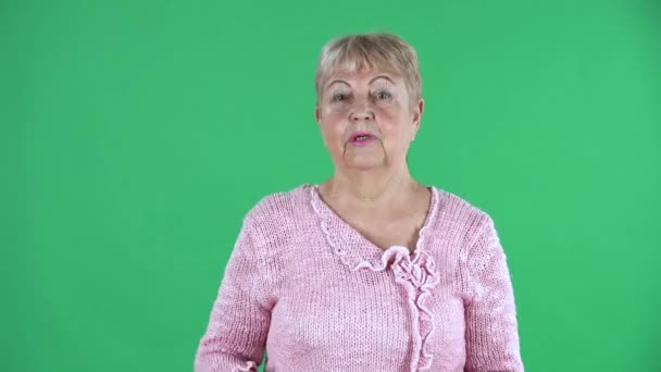 Портрет літньої жінки, яка дивиться на камеру, емоційно розмовляє з людиною, яка обурюється. Бабуся з коротким волоссям в рожевому светрі на зеленому екрані в студії. Зачиніть.. — стокове відео