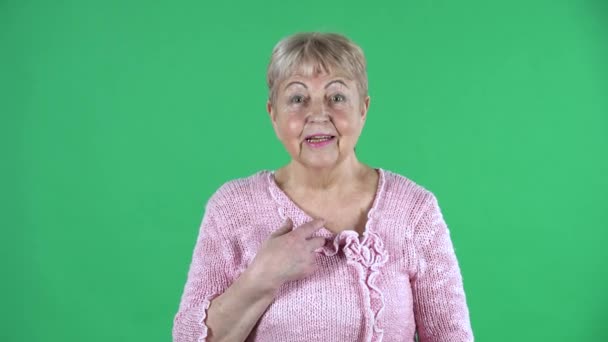 Retrato mulher idosa olhando para a câmera e fazendo um gesto não, não sou eu. Avó de cabelos grisalhos com cabelo curto em um suéter rosa na tela verde no estúdio. Fechar. — Vídeo de Stock