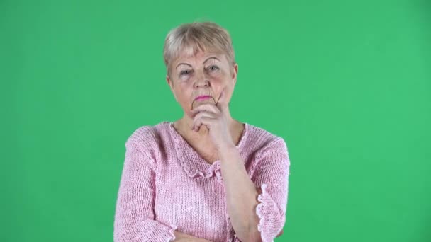 Porträtt äldre kvinna tänker med koncentration upprörd ingen aning. Grå hårig mormor med kort hår i en rosa tröja på grön skärm i studio. Närbild. — Stockvideo