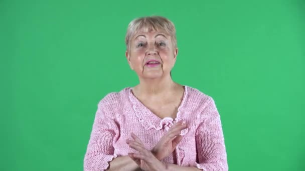Portré idős nő szigorúan gesztikulál a kezét keresztbe így X alakú jelentése tagadás nemet mond. Ősz hajú nagymama, rövid hajjal, rózsaszín pulóverben, zöld vásznon a stúdióban. Közelről.. — Stock videók