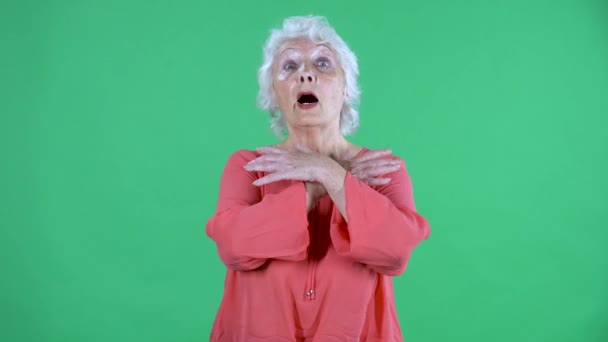 Portret van een oudere vrouw die naar de camera kijkt met een geschrokken bange uitdrukking en emotioneel gebaar met haar handen. Grijze oma in rode blouse op groen scherm in de studio. Sluiten.. — Stockvideo