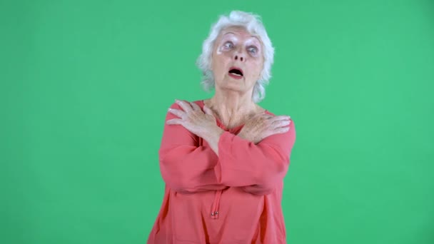 Portrait einer älteren Frau, die mit schockiertem, verängstigtem Gesichtsausdruck in die Kamera blickt und die Arme über der Brust verschränkt. Grauhaarige Großmutter in roter Bluse auf grünem Bildschirm im Studio. Nahaufnahme. — Stockvideo