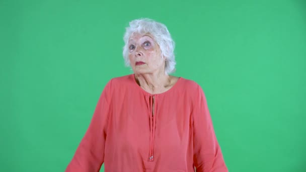 Retrato mulher idosa olhando para a câmera encolhe os ombros não sei. Avó de cabelos grisalhos em blusa vermelha na tela verde no estúdio. Fechar. — Vídeo de Stock