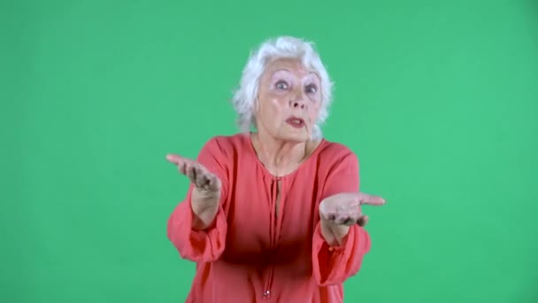 Portrait einer älteren Frau, die empört mit den Händen in die Kamera blickt. Grauhaarige Großmutter in roter Bluse auf grünem Bildschirm im Studio. Nahaufnahme. — Stockvideo