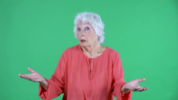 Porträtt äldre kvinna tittar på kameran skakar hans huvud det är inte jag, jag vet inte vad som händer. Grå hårig mormor i röd blus på grön skärm i studio. Närbild. — Stockvideo