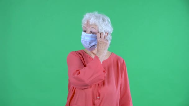 Portrait einer älteren Frau, die in die Kamera blickt und die medizinische Maske abnimmt. Grauhaarige Großmutter in roter Bluse auf grünem Bildschirm im Studio. Nahaufnahme. — Stockvideo