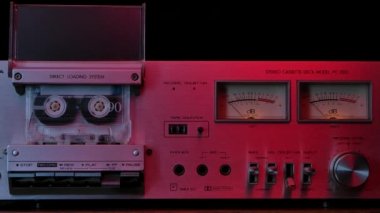 80 'lerin klasik kaset çalar güvertesi kırmızı neon ışıklarla aydınlatılmış. Teybi dönen kaset, kontroller, gösterge paneli ve siyah arka planda düğmeleri olan ses kaydedici. Kapatın. Yavaş çekim.