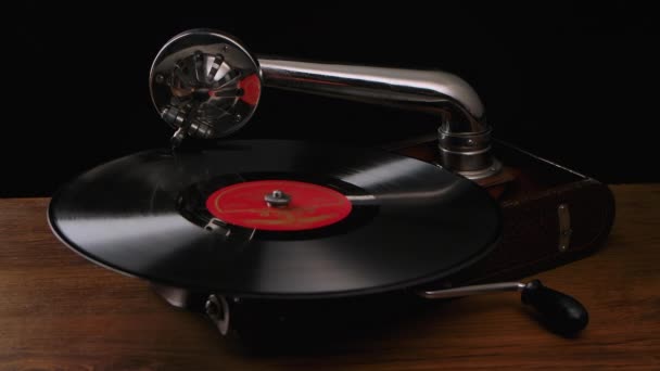 Przenośny, stary gramofon z igłą na wirującej płycie winylowej. Vintage instrument muzyczny na drewnianym stole w ciemnym studio. Zwolnij trochę. Zamknij się.. — Wideo stockowe