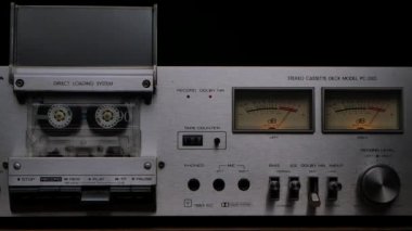 80 'lerin klasik kaset çalar destesi. Teybi dönen kaset, kontroller, gösterge paneli ve siyah arka planda düğmeleri olan ses kaydedici. Kapatın. Yavaş çekim.