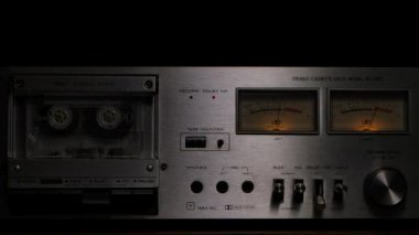 80 'lerin klasik kaset çalar destesi. Teybi dönen kaset, kontroller, gösterge paneli ve siyah arka planda düğmeleri olan ses kaydedici. Kapatın. Yavaş çekim.