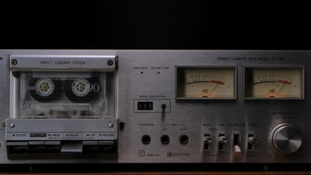 Dek pemutar kaset kuno dari tahun 80-an. Stereo recorder dengan kaset berputar, kontrol, dashboard dan tombol di latar belakang studio hitam. Tutup. Gerakan lambat. — Stok Video