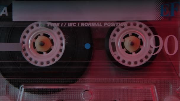 Retro compact audio cassette playing extreme close up. Vintage music cassette playing back in the player illuminated by red neon lights. Slow motion. — Stock Video