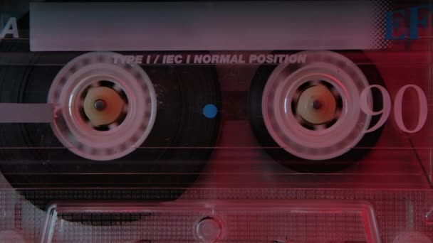 Vintage casete de audio compacto extrema de cerca. Casete de música retro en los rebobinados iluminados por luces de neón rojas. Movimiento lento. — Vídeos de Stock