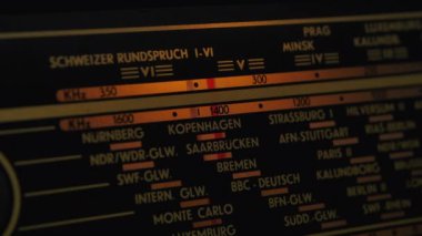 Eski bir radyo kanalı, farklı radyo frekanslarında istasyonları arıyor. Antika ahşap radyo alıcısı karanlıkta parlar. Ön panel kapanıyor..