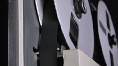 Eski teyp üzerinde dönen makaralar. Manyetik bandı vurguluyorum. Retro konsept döner makara teypten makaraya. Eski müzik için nostalji. Karanlık bir stüdyoda yakın çekim..