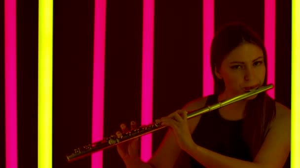 Solo kinerja dari pemain seruling di konser jazz. Musisi wanita profesional muda melakukan pertunjukan dengan latar belakang lampu neon terang. Siluet. Tutup. Gerakan lambat. — Stok Video