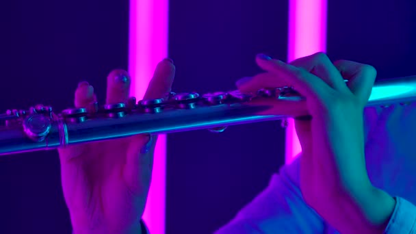 古典音乐交响乐音乐会,由一名专业的长笛演奏家表演.女性的手紧紧抓住长笛的琴键。在明亮的紫色霓虹灯背景下的管乐器.慢动作 — 图库视频影像