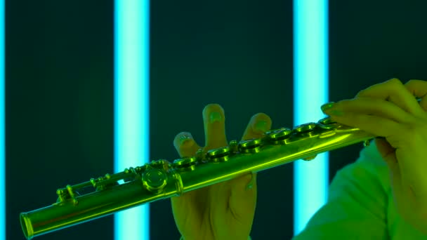 Virtuoso performance of professional flutist in the musical theater orchestra. Female hands with a flute close up. Wind instrument against background of bright multicolored neon lights. Slow motion. — Stock Video