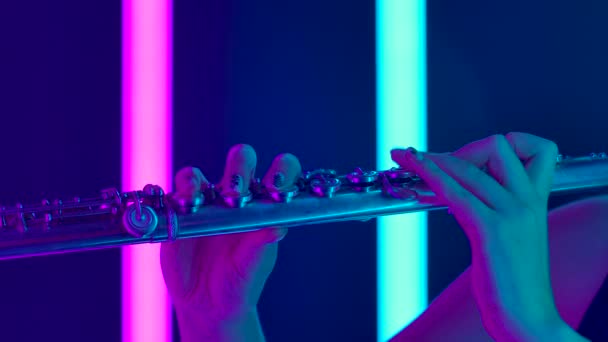 プロのフルート奏者によるクラシック音楽のシンフォニーコンサート。笛の女性の手のタッチキーを閉じます。明るい紫色のネオンライトを背景にした管楽器。スローモーション — ストック動画