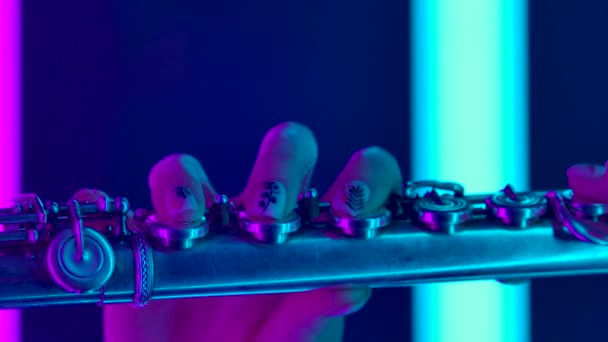 Flauto in mani femminili vicino. Professionale musicista femminile suona un concerto classico sullo sfondo di luci al neon luminose. Poster per una scuola di musica. Rallentatore. — Video Stock